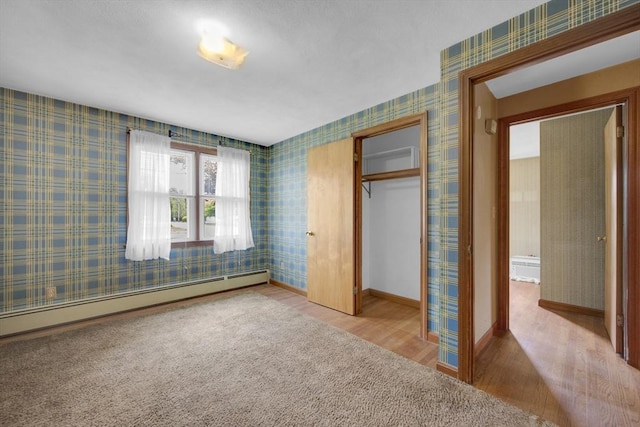 1032 Tinkham Rd, Wilbraham, MA 01095 - unfurnished bedroom featuring wood finished floors, baseboard heating, a closet, baseboards, and wallpapered walls