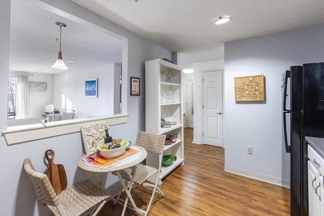 kitchen featuring black refrigerator, hanging light fixtures, and hardwood / wood-style flooring