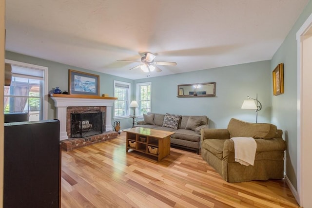 living room with a ceiling fan, light wood-type flooring, a fireplace, and baseboards