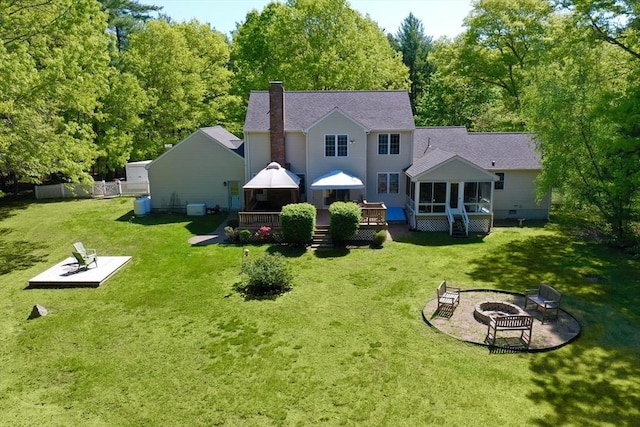rear view of property with an outdoor fire pit, a sunroom, a deck, a chimney, and a lawn