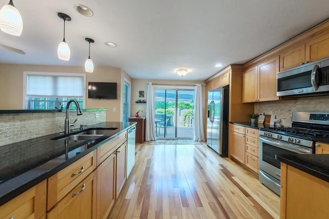 kitchen with stainless steel appliances, a sink, backsplash, decorative light fixtures, and light wood finished floors