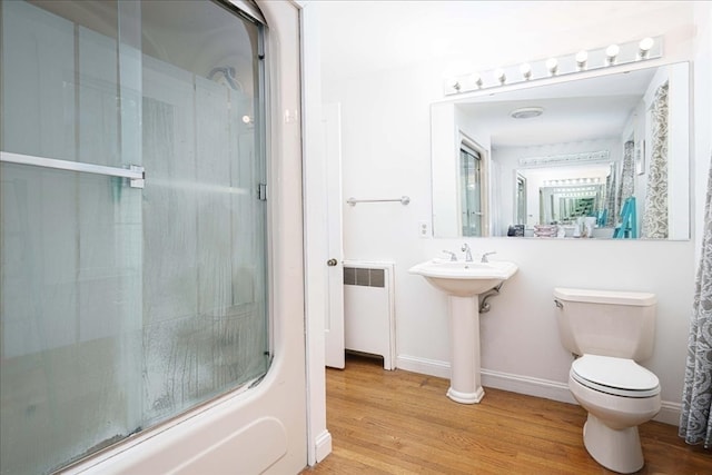 full bathroom with shower / bath combination with glass door, sink, radiator heating unit, wood-type flooring, and toilet