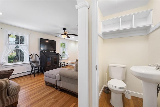 bathroom featuring wood finished floors, toilet, baseboards, ceiling fan, and a sink