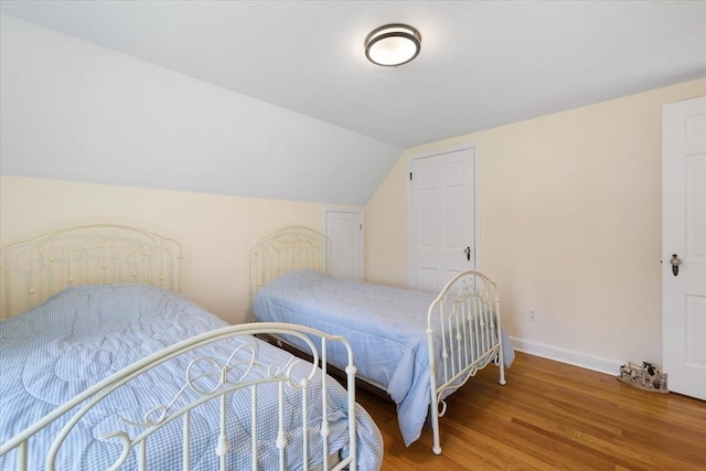 bedroom with baseboards, vaulted ceiling, and wood finished floors