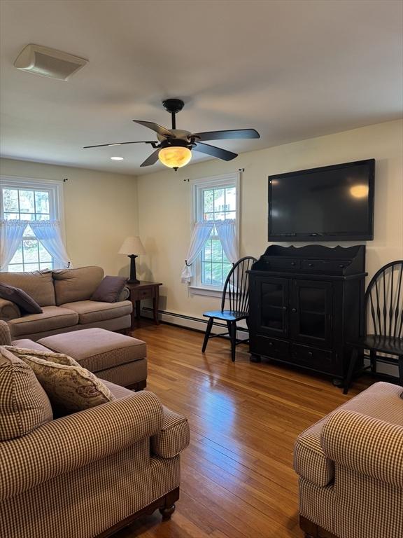 living room featuring wood finished floors, a ceiling fan, and a baseboard heating unit