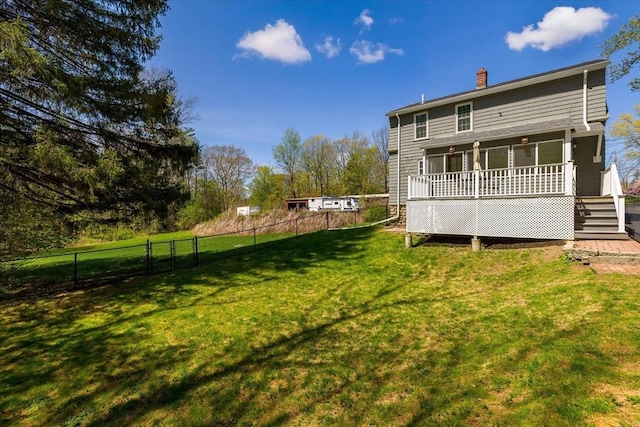 rear view of property with a chimney, a lawn, a wooden deck, stairway, and fence
