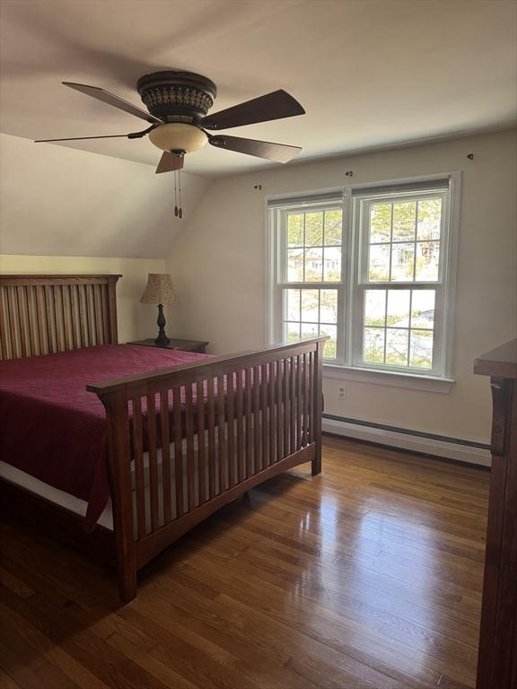 bedroom featuring a ceiling fan, a baseboard heating unit, wood finished floors, and vaulted ceiling