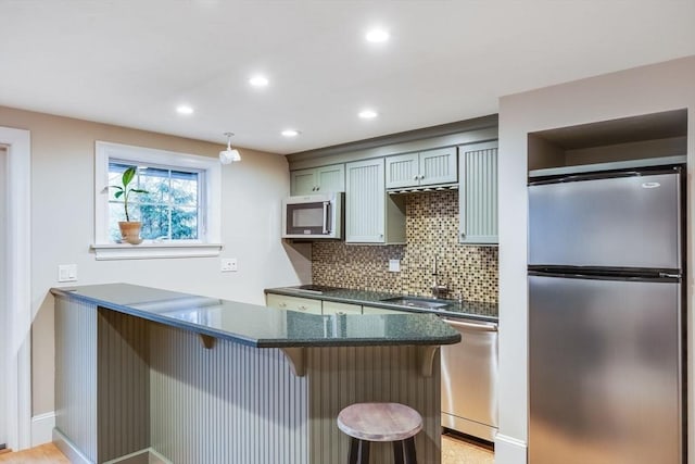 kitchen featuring backsplash, dark stone counters, a kitchen breakfast bar, sink, and appliances with stainless steel finishes