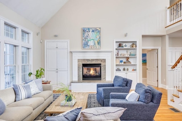 living room with light hardwood / wood-style floors, a premium fireplace, a healthy amount of sunlight, and high vaulted ceiling