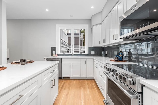 kitchen with white cabinetry, decorative backsplash, light hardwood / wood-style flooring, and stainless steel appliances