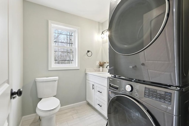 laundry area featuring baseboards, stacked washer and clothes dryer, light wood-type flooring, and laundry area