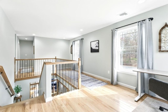 hall with an upstairs landing, a wealth of natural light, visible vents, and wood finished floors