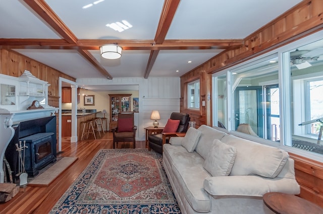 living room featuring a wood stove, beamed ceiling, hardwood / wood-style flooring, ornate columns, and ceiling fan