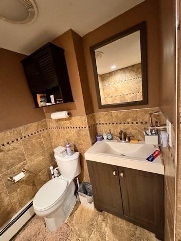 139 Westmoor Rd, Boston, MA 02132 - bathroom with baseboard heating, tile walls, vanity, and a wainscoted wall