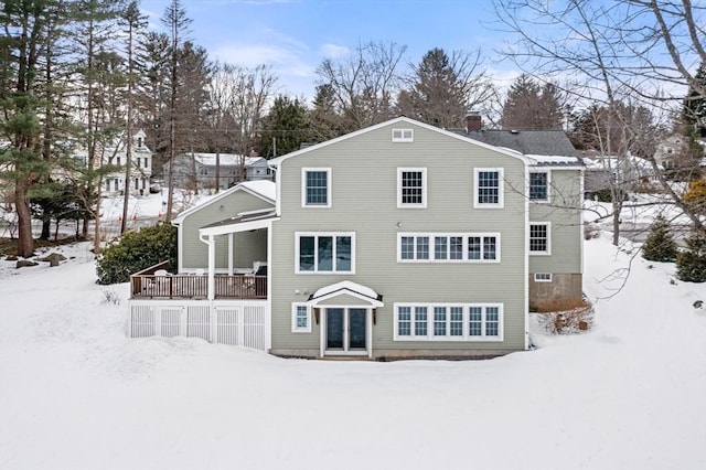 snow covered rear of property featuring a wooden deck and a chimney