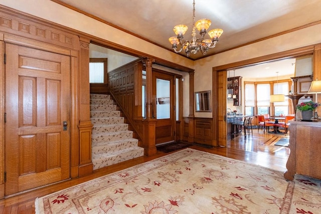 foyer with an inviting chandelier, stairs, ornamental molding, and wood finished floors