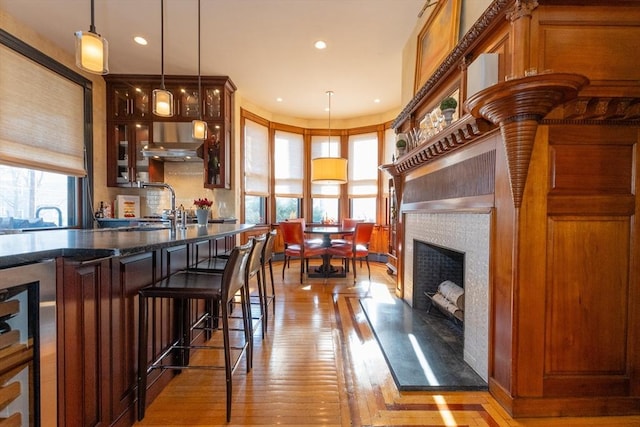 kitchen with pendant lighting, a tiled fireplace, glass insert cabinets, light wood-style floors, and a sink