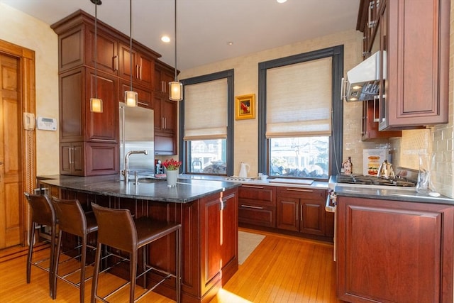 kitchen with light wood finished floors, tasteful backsplash, a breakfast bar area, built in refrigerator, and extractor fan