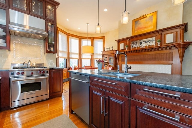 kitchen with under cabinet range hood, a sink, appliances with stainless steel finishes, light wood finished floors, and decorative light fixtures