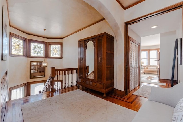 hall featuring baseboards, ornamental molding, wood finished floors, and an upstairs landing