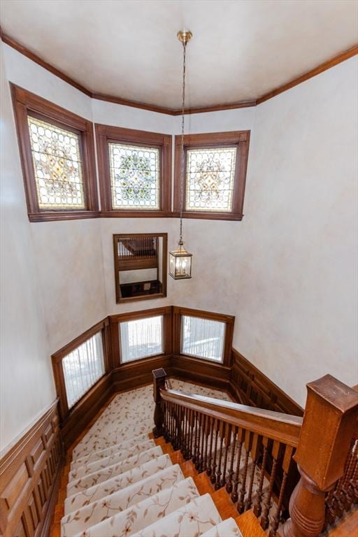 stairs with wainscoting, crown molding, and wood finished floors