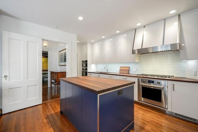 kitchen with wood counters, white cabinetry, wall chimney exhaust hood, and hardwood / wood-style flooring