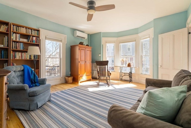 living area with ceiling fan, a wall unit AC, and wood finished floors