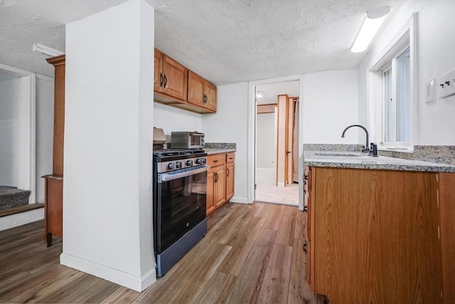 6 Hillside Rd, Holland, MA 01521 - kitchen with stainless steel gas stove, a sink, light wood-style floors, a textured ceiling, and brown cabinetry