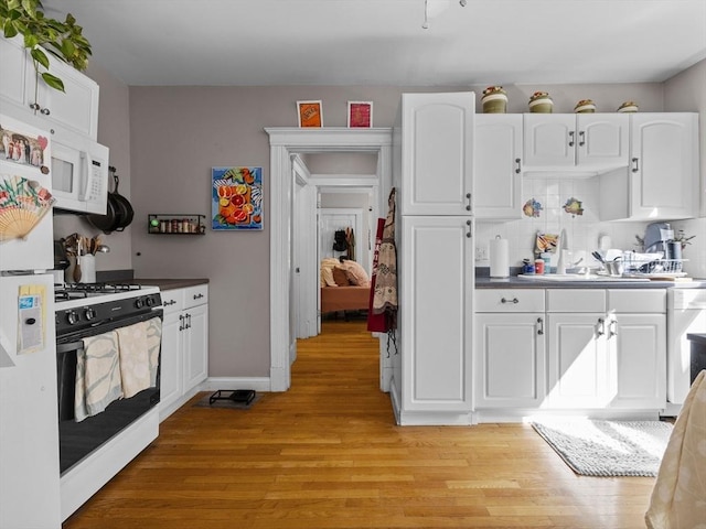 kitchen featuring freestanding refrigerator, white cabinets, gas range oven, dark countertops, and light wood-type flooring