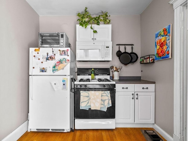 kitchen with white appliances, baseboards, light wood finished floors, a toaster, and dark countertops