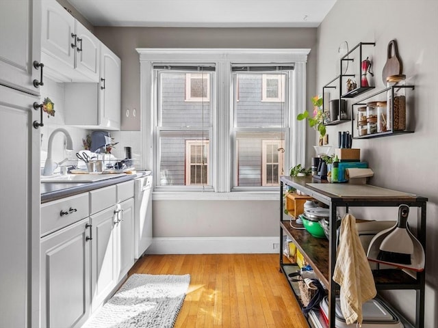 kitchen featuring a sink, dark countertops, white cabinetry, light wood-style floors, and baseboards