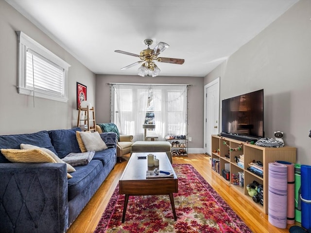 living room featuring baseboards, light wood-type flooring, and ceiling fan