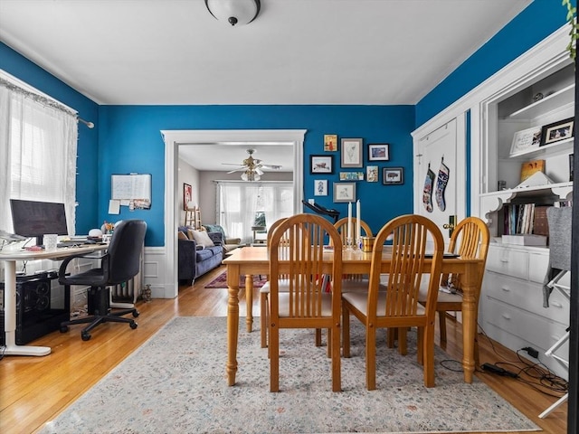 dining space with a ceiling fan, wood finished floors, and wainscoting