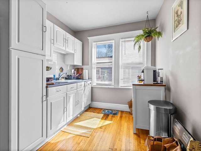 kitchen featuring light wood finished floors, backsplash, baseboards, white cabinetry, and a sink