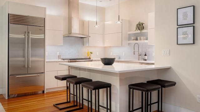 kitchen featuring stainless steel built in refrigerator, extractor fan, a breakfast bar area, and white cabinets