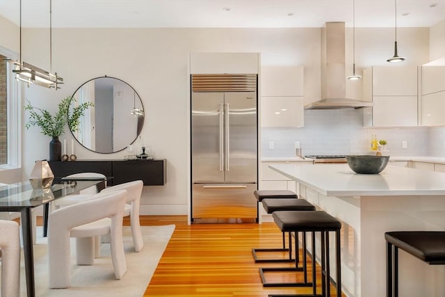 kitchen featuring white cabinetry, stainless steel built in refrigerator, pendant lighting, and exhaust hood