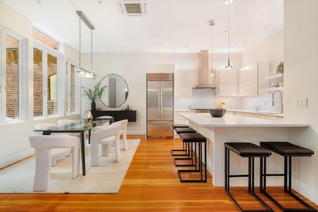 kitchen featuring sink, white cabinetry, range hood, decorative light fixtures, and built in fridge