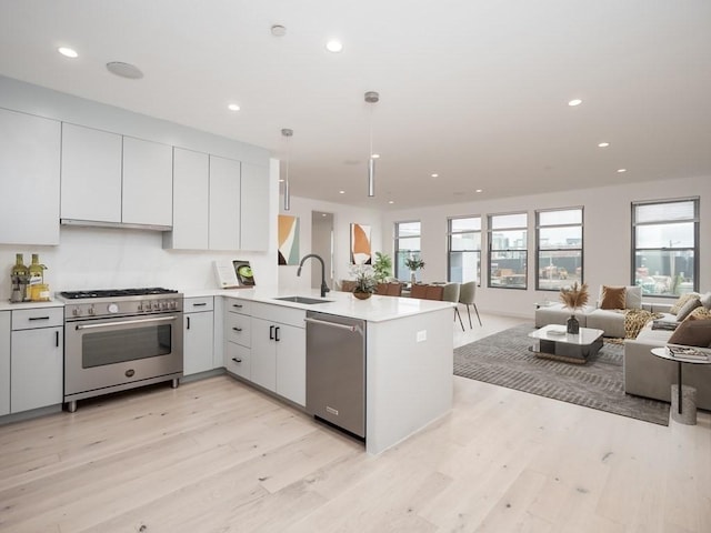 kitchen with sink, hanging light fixtures, light hardwood / wood-style flooring, kitchen peninsula, and appliances with stainless steel finishes