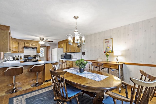 dining room with light wood-type flooring, wallpapered walls, a chandelier, and a ceiling fan