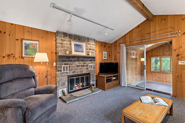 carpeted living area with vaulted ceiling, track lighting, wooden walls, and a stone fireplace
