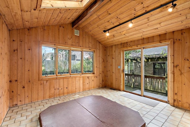 empty room with track lighting, healthy amount of natural light, vaulted ceiling, wood walls, and a skylight