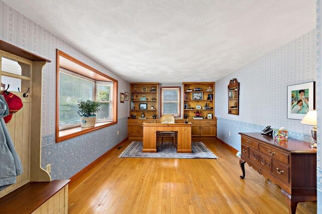 office area featuring wallpapered walls, light wood-style flooring, and a textured ceiling