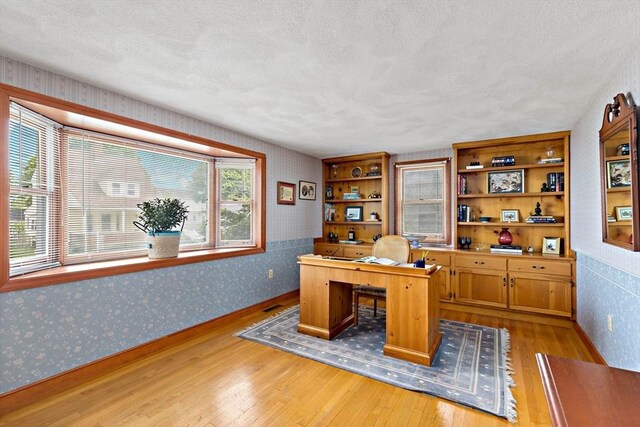 home office with hardwood / wood-style floors, wallpapered walls, and a textured ceiling