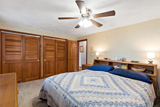 bedroom with wallpapered walls, two closets, carpet, and a ceiling fan