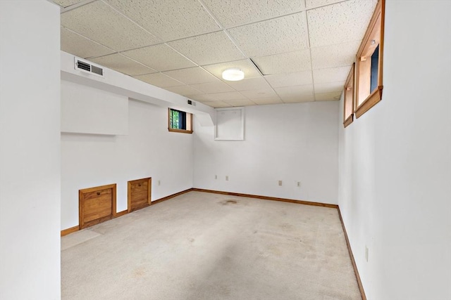 below grade area with baseboards, a drop ceiling, and light colored carpet