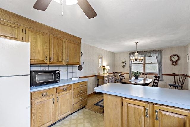 kitchen featuring freestanding refrigerator, black microwave, light countertops, ceiling fan, and a chandelier