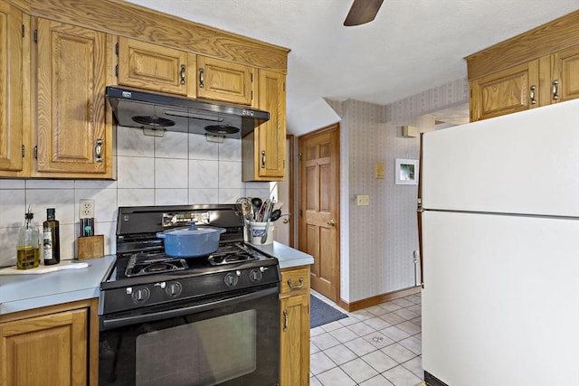 kitchen featuring freestanding refrigerator, gas stove, under cabinet range hood, light countertops, and baseboards