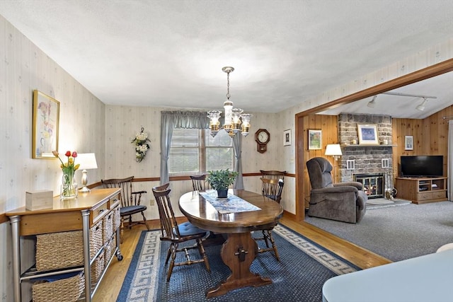 dining room with wood finished floors, a chandelier, a stone fireplace, and wood walls