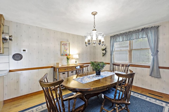 dining area with a chandelier, wood finished floors, baseboards, and wallpapered walls