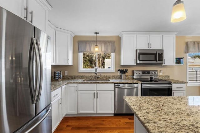 kitchen with hanging light fixtures, white cabinetry, sink, and stainless steel appliances